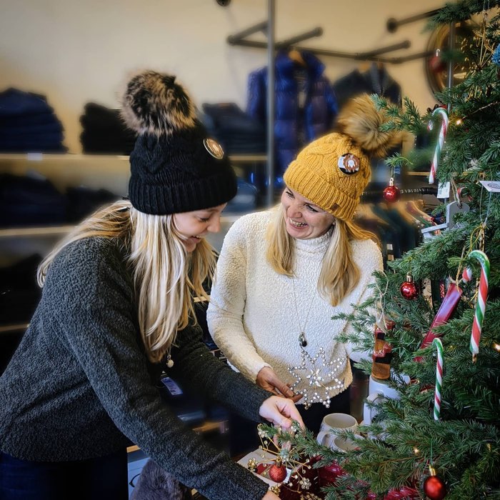 two women in toques laughing next to a christmas tree.