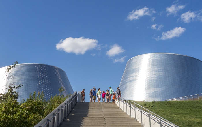 people standing at the top of an outdoor staircase between two large shiny cylindrical structures