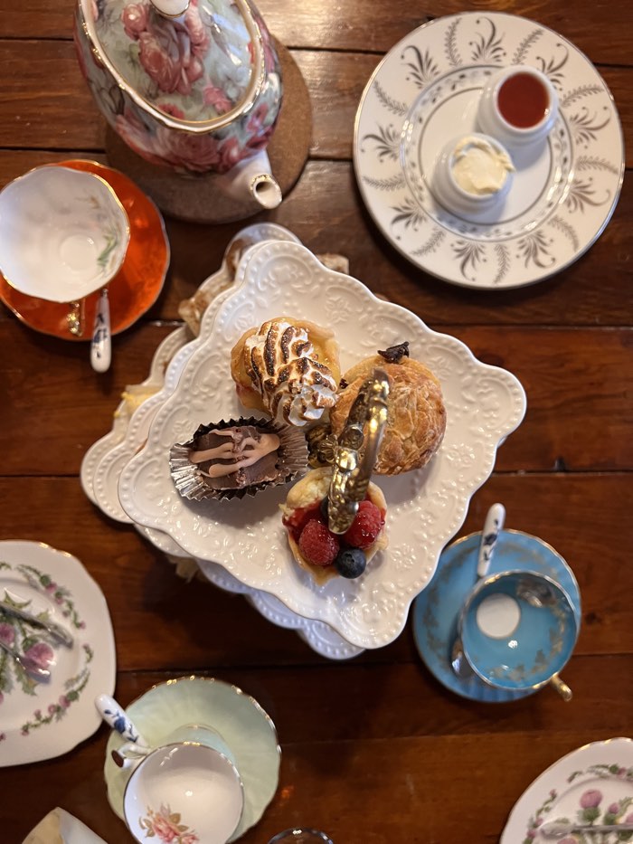 photo of petit fours on a white plate surrounded by teapot, teacups, butter and jam