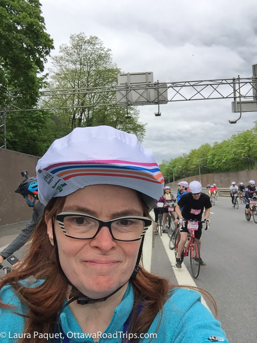 woman in a bike helmet on a wide road with cyclists in background on the five boro bike tour in new york city
