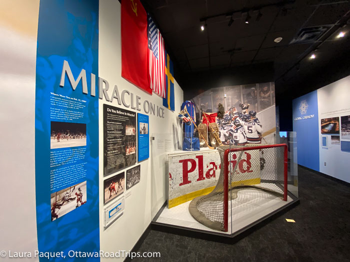 lake placid olympic museum exhibit with photos, american and soviet union flags, and a hockey net from the 1980 miracle on ice game.