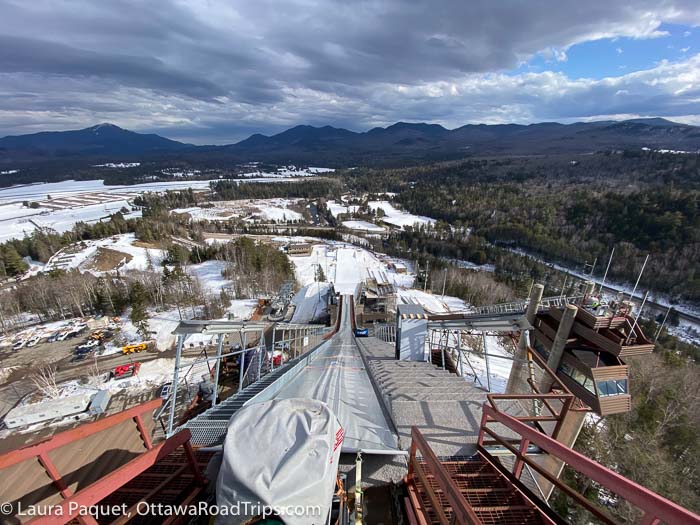 view of mountains and trees from the top of the steep ski jump ramp at the olympic jumping complex in lake placid, new york.