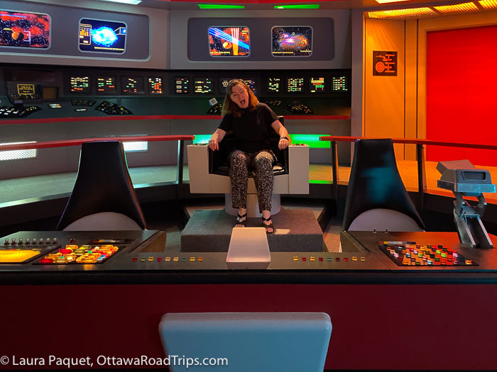 woman sitting in captain's chair in replica of the bridge from Star Trek TOS, pretending to scream in terror