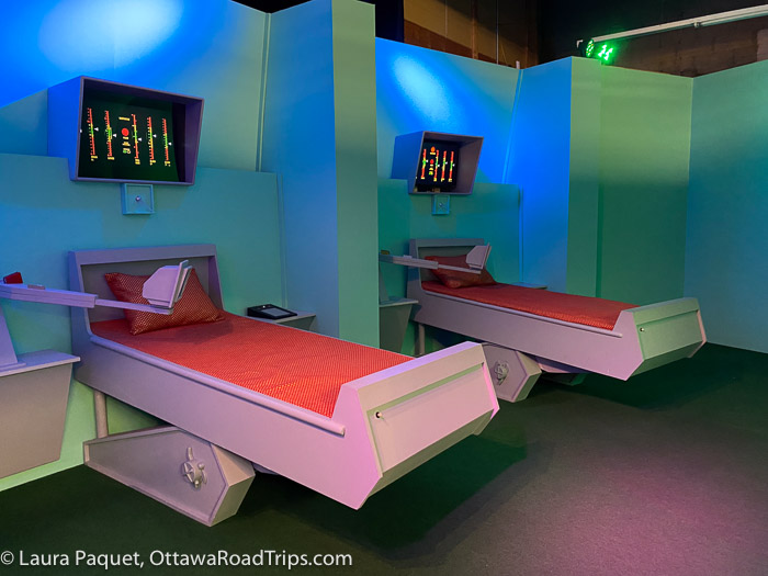 two bed with orange sheets and pillows, with computer monitors above them, in replica star trek tos sickbay