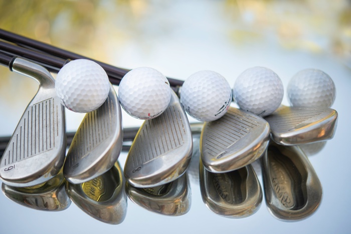 closeup of golf irons and golf balls on mirrored surface