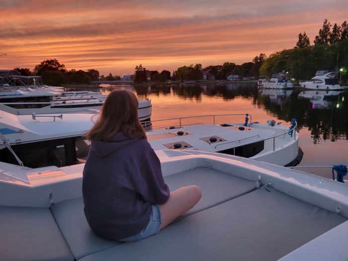 woman sitting on boat deck looking out at a marina at sunset