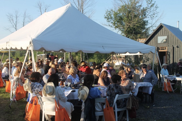 people sitting at round tables with cloth tablecloths under a white marquee in a field