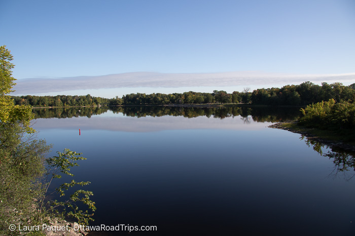 small, calm lake surrounded by trees, with a beach in the background, at lac leamy.