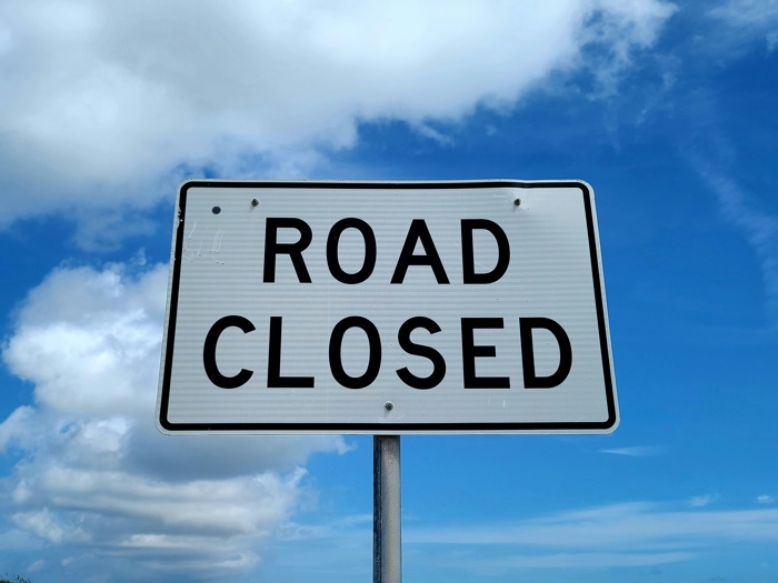 black and white sign reading "road closed" against blue sky and clouds