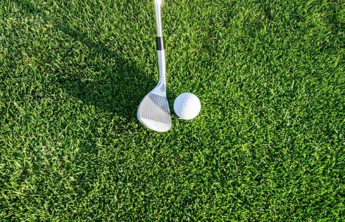 close up of a golf club head beside a golf ball on a green