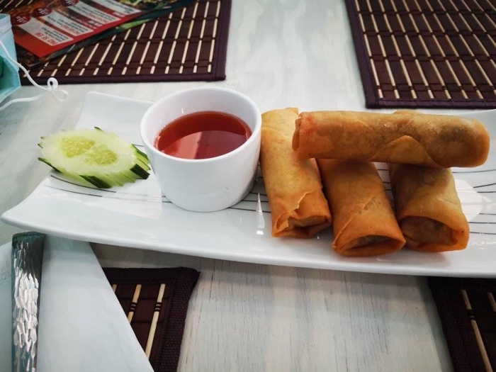 spring rolls on a white plate with cucumber slices and dipping sauce