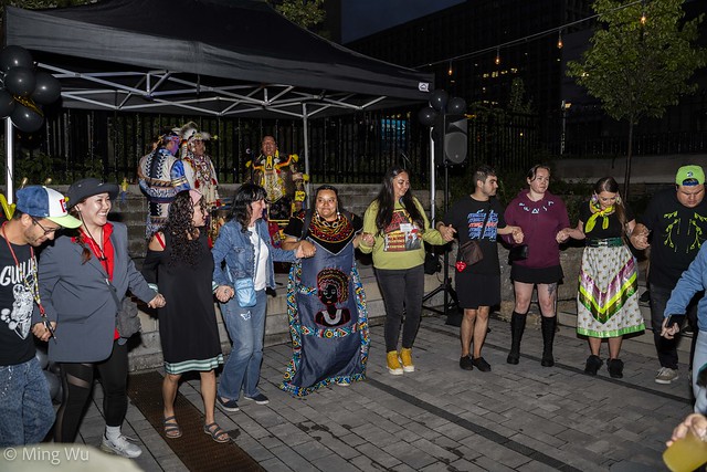 people, some in indigenous clothing, dancing in a circle at night