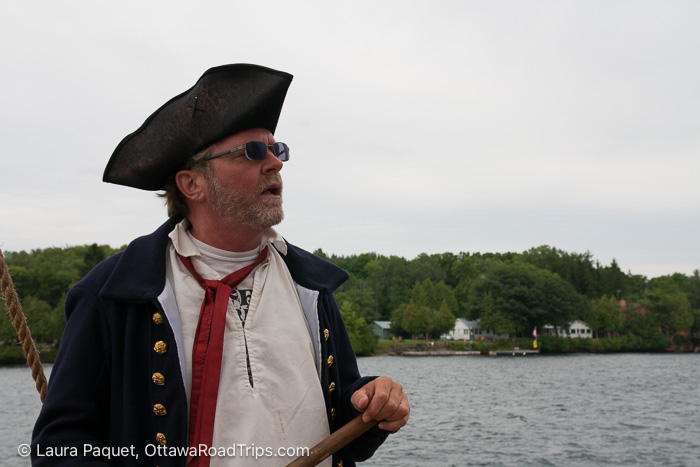 man in historical ship captain costume on deck of tall ship with river behind