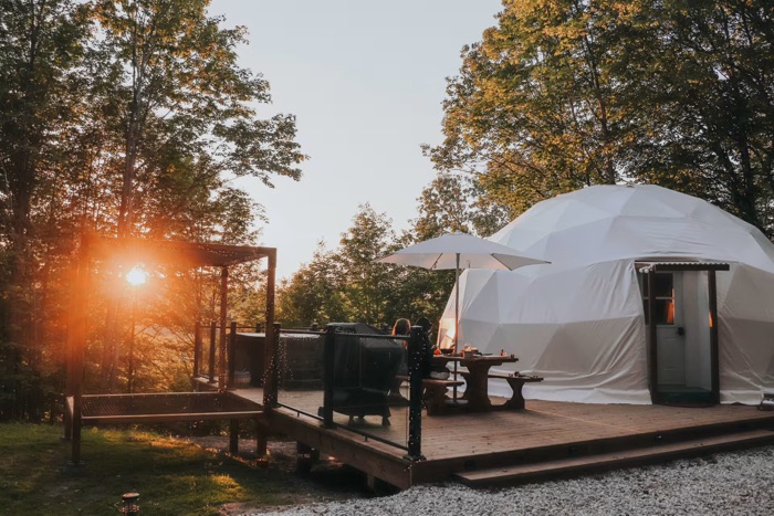 domed semi-permanent white tent with terrace surrounded by trees at sunset