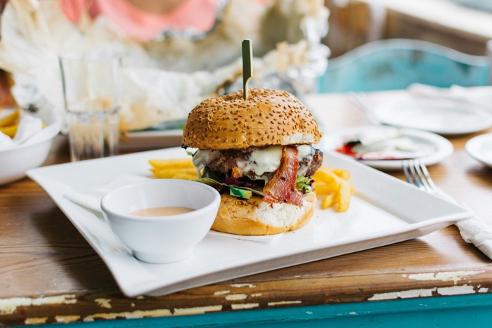 large hamburger and a small bowl of sauce on a square white plate