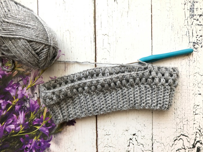 grey yarn and a small bit of crocheting on a white wooden table