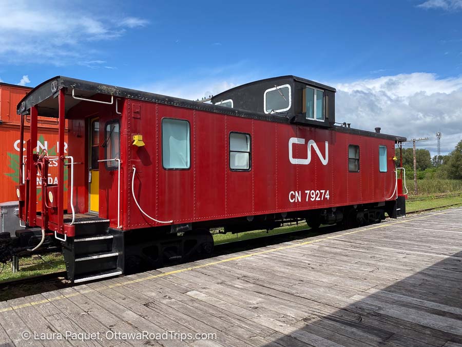 red 1967 cn caboose parked next to a wooden train platform at the railway museum of eastern ontario in smiths falls.