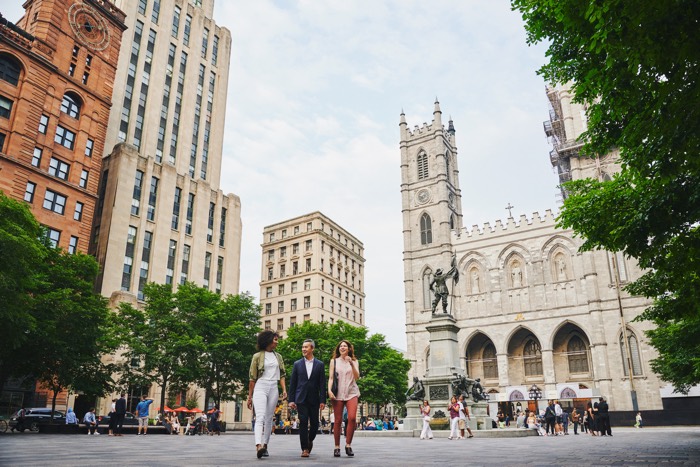 three people walking toward camera in front of notre-dame basilica in old montreal.