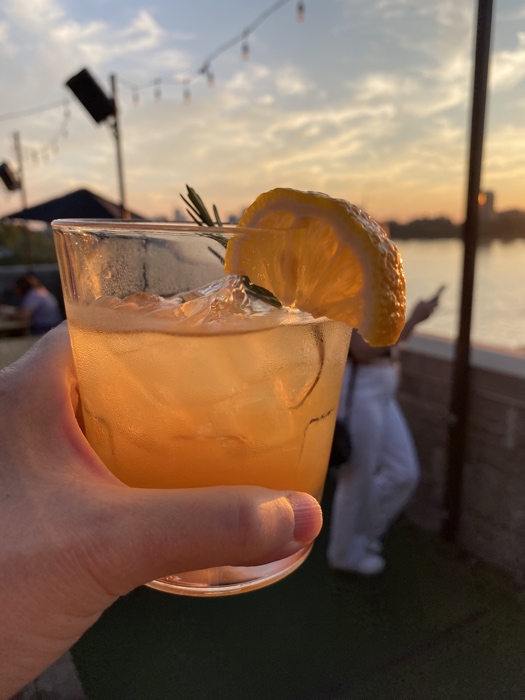 hand holding a glass of orange cocktail with sunset in background