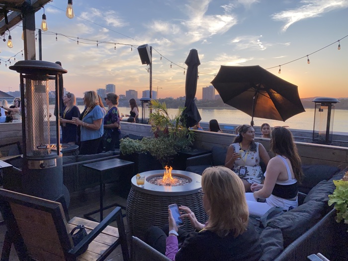 people sitting on couches around fire tables with sunset in background at tavern on the falls.