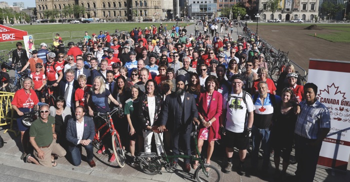 A crowd of people, some with bikes, standing outside on Parliament Hill in Ottawa.
