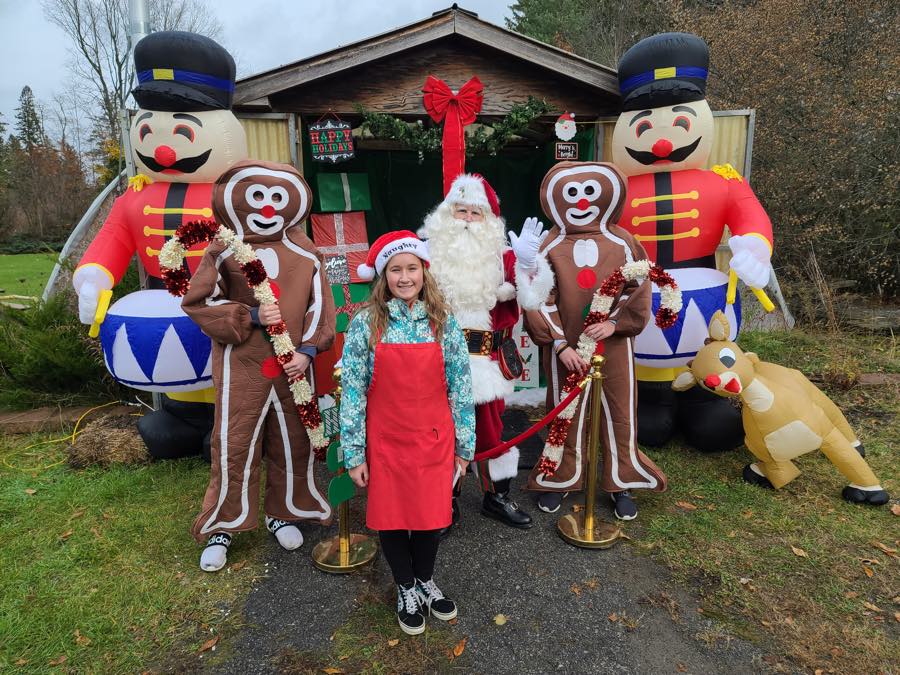 girl with santa and inflatable gingerbread men, nutcrackers and reindeer in front of decorated shed