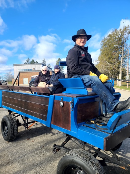 man in cowboy hat driving blue wagon with two women in back.