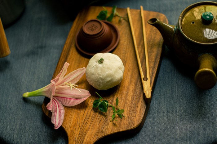 small white ball of mochi with flowers and herbs on a wooden board, next to a small teapot