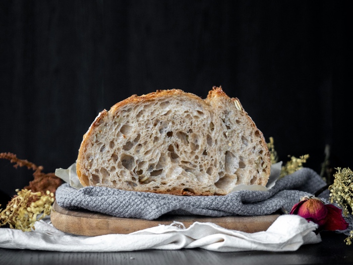 cut loaf of rustic bread on a cutting board, surrounded by dried  herbs