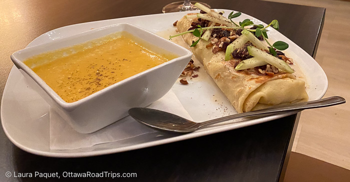 square bowl of soup and a crepe topped with apples and nuts on a white plate