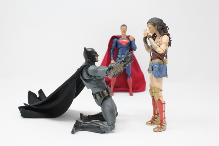 three action figures; batman appears to be proposing to wonder woman, and superman is angry