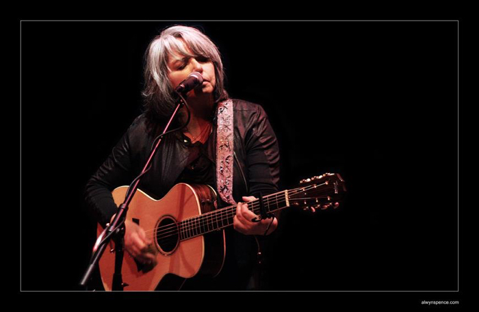 woman in a leather jacket at a microphone playing an acoustic guitar