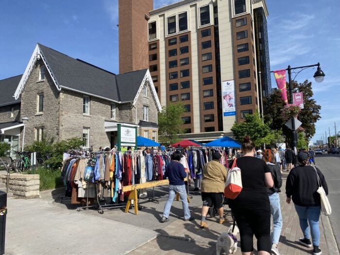 great glebe garage sale 2024 - Ottawa Road Trips people browsing and walking past racks of clothes in front of abbotsford house in the glebe