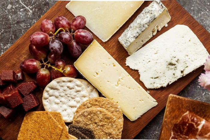 edward-howell-cheese-700-unsplash - Ottawa Road Trips photo of a cheese board with soft and hard cheeses, crackers and grapes