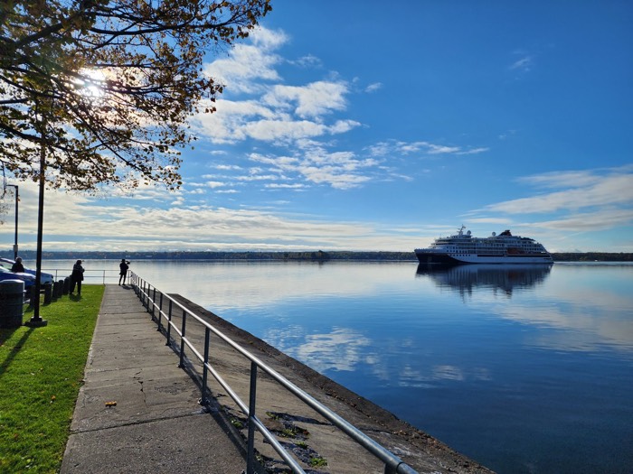 people on a concrete path looking at a small cruise ship on a river