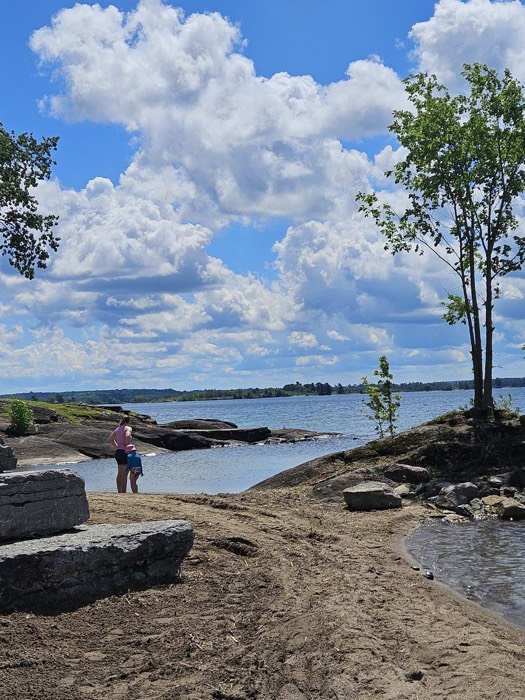 woman and small child on a beach looking out on a rocky shoreline.