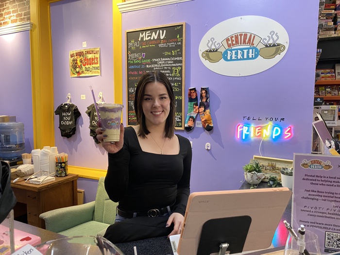 woman holding a smoothie in front of a wall decorated with friends items