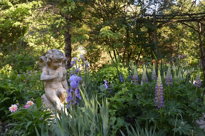 sculpture of a cherub in a garden, surrounded by pink and purple flowers