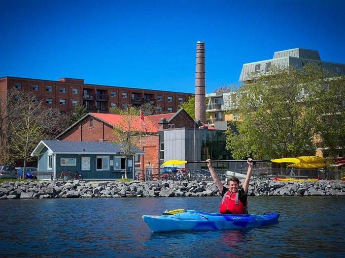smiling person in a blue kayak with city buildings in background