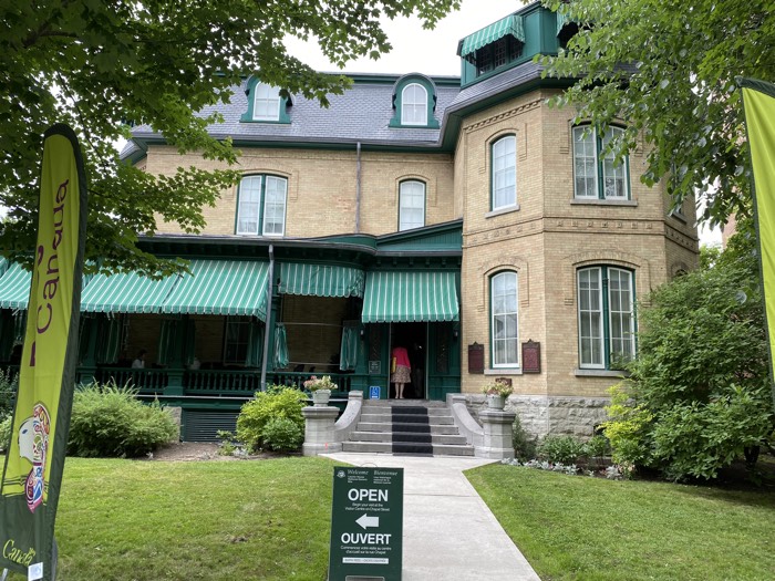 exterior of laurier house, a yellow-brick second empire home with green-and-white striped awnings