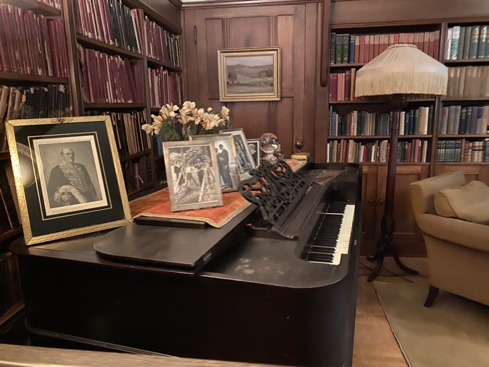 piano topped with photos and a crystal ball in a room lined with bookshelves