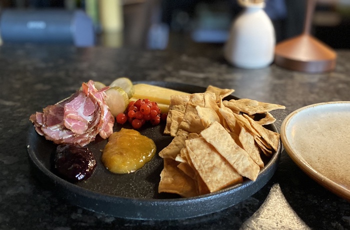 round black plate with cured meats, cheese, pickles, crackers and condiments