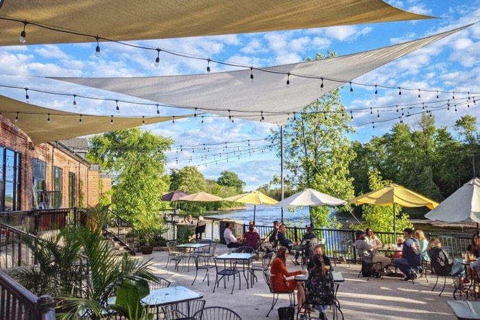 people eating under awnings and patio umbrellas on a patio overlooking a river