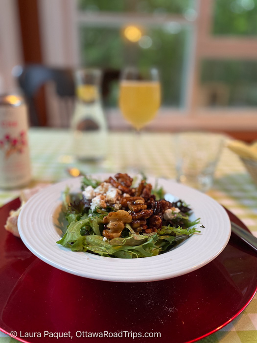 green salad with pecans and feta in a white bowl on a red charger plate