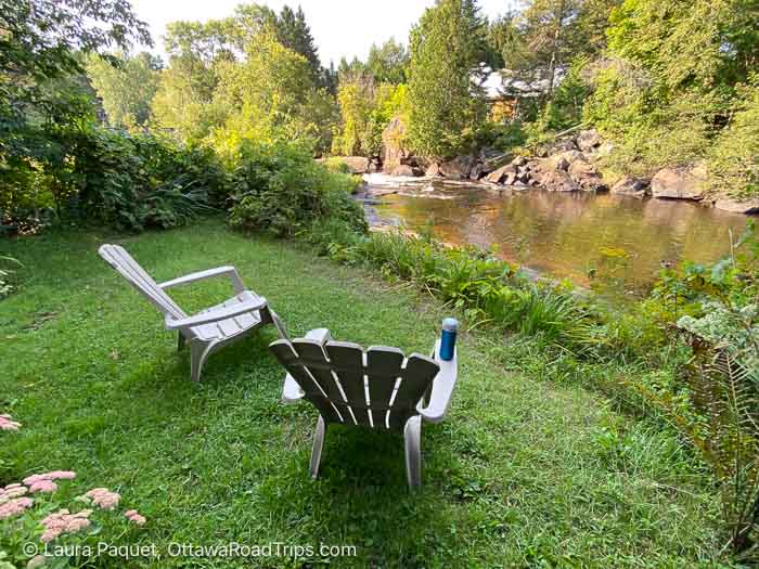 two plastic muskoka chairs on a lawn beside a river