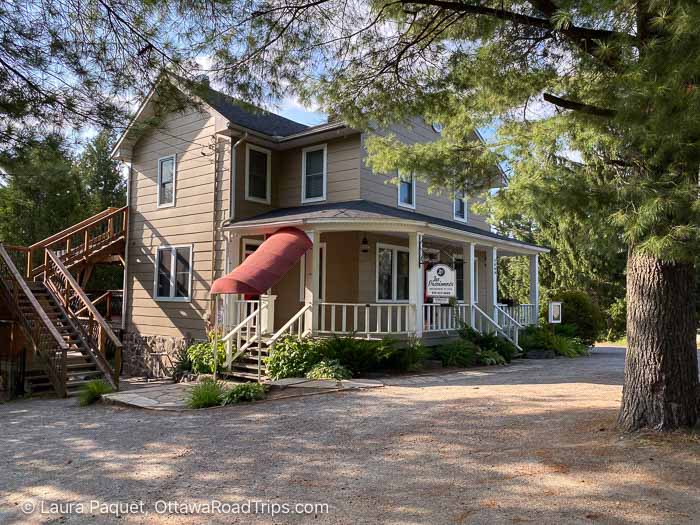 brown wooden house with wraparound porch, surrounded by trees