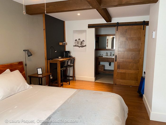 guest room with a bed, desk, wooden roof beams, sliding barn door to bathroom