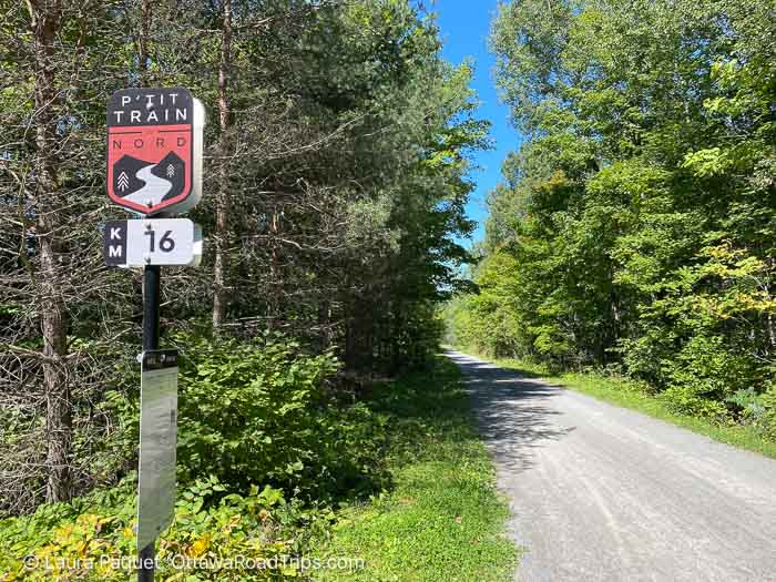 signpost reading 16km beside a crushed stone trail with trees on both sides