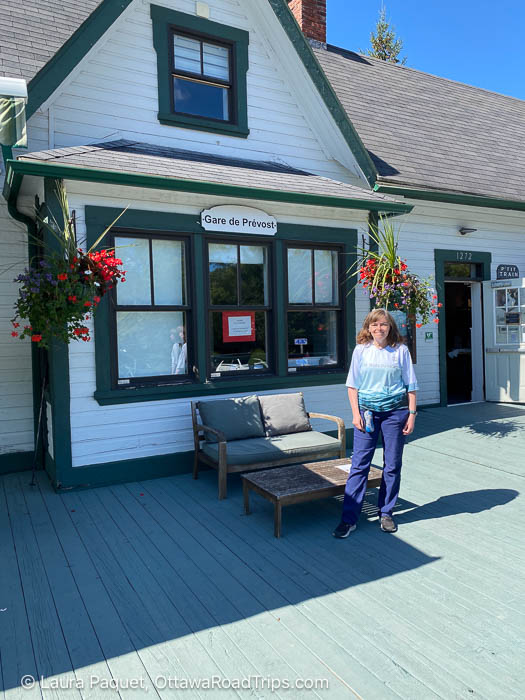 smiling woman in front of a small white train station with green trim
