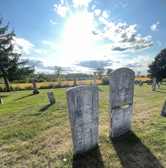 grey headstones of john and mary miller with sun shining behind them